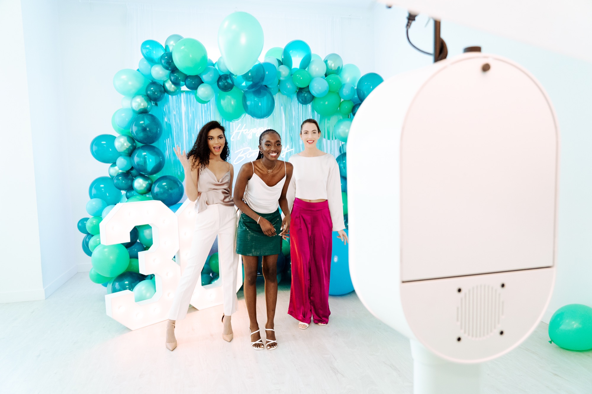 Three friends posing at a 30th birthday party with balloon arch backdrop