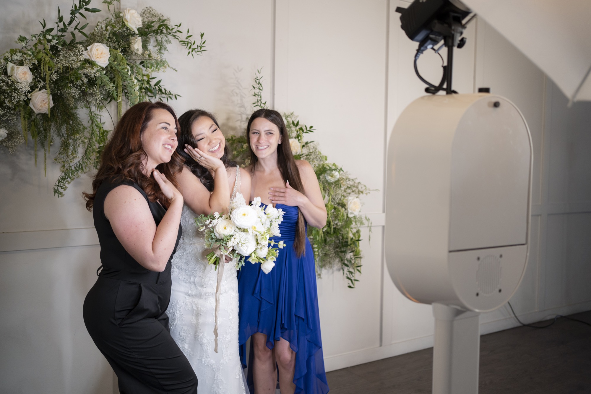 Bride and bridesmaids laughing at the photo booth with floral backdrop